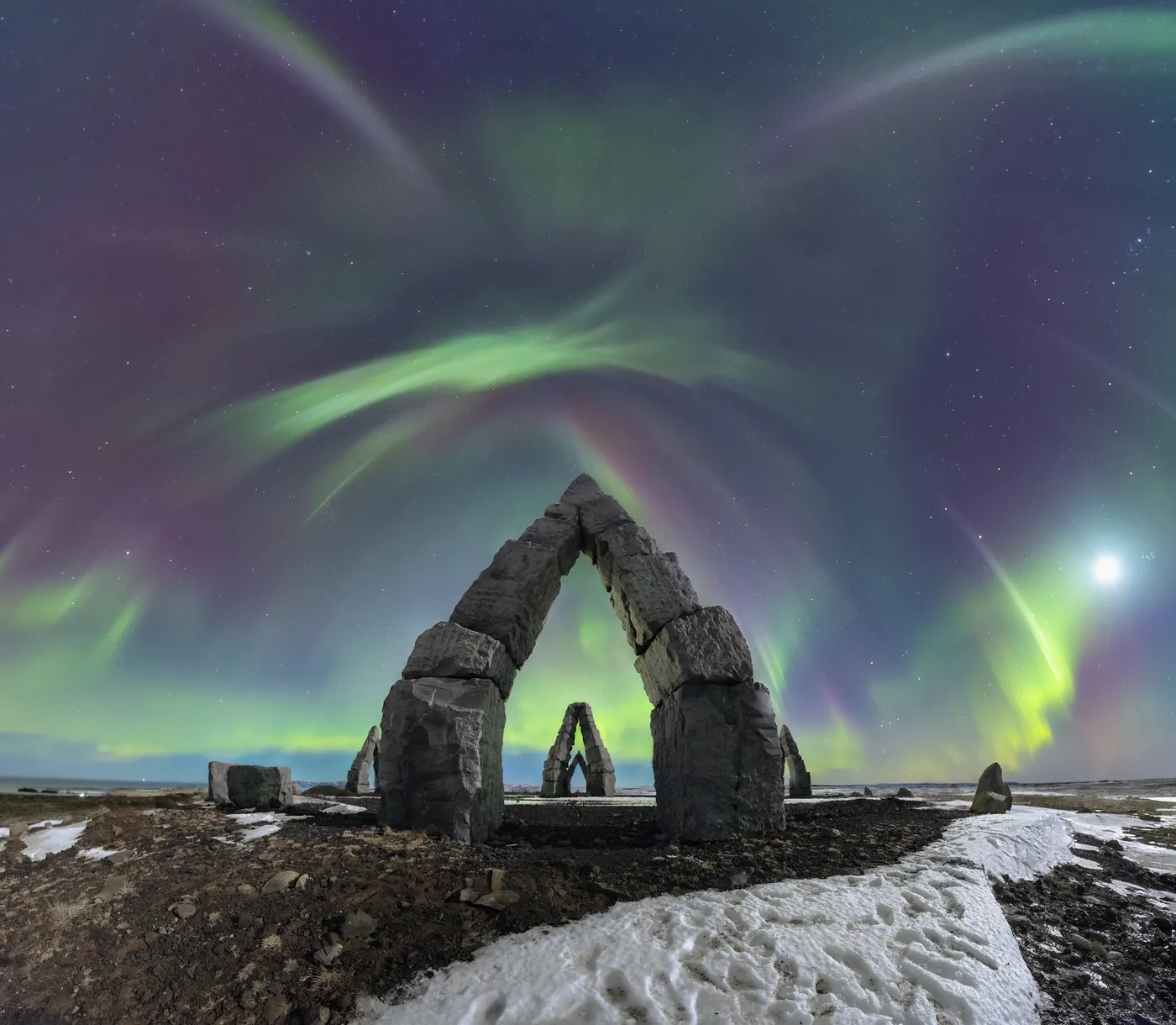 A stone arch under violet and green aurora.