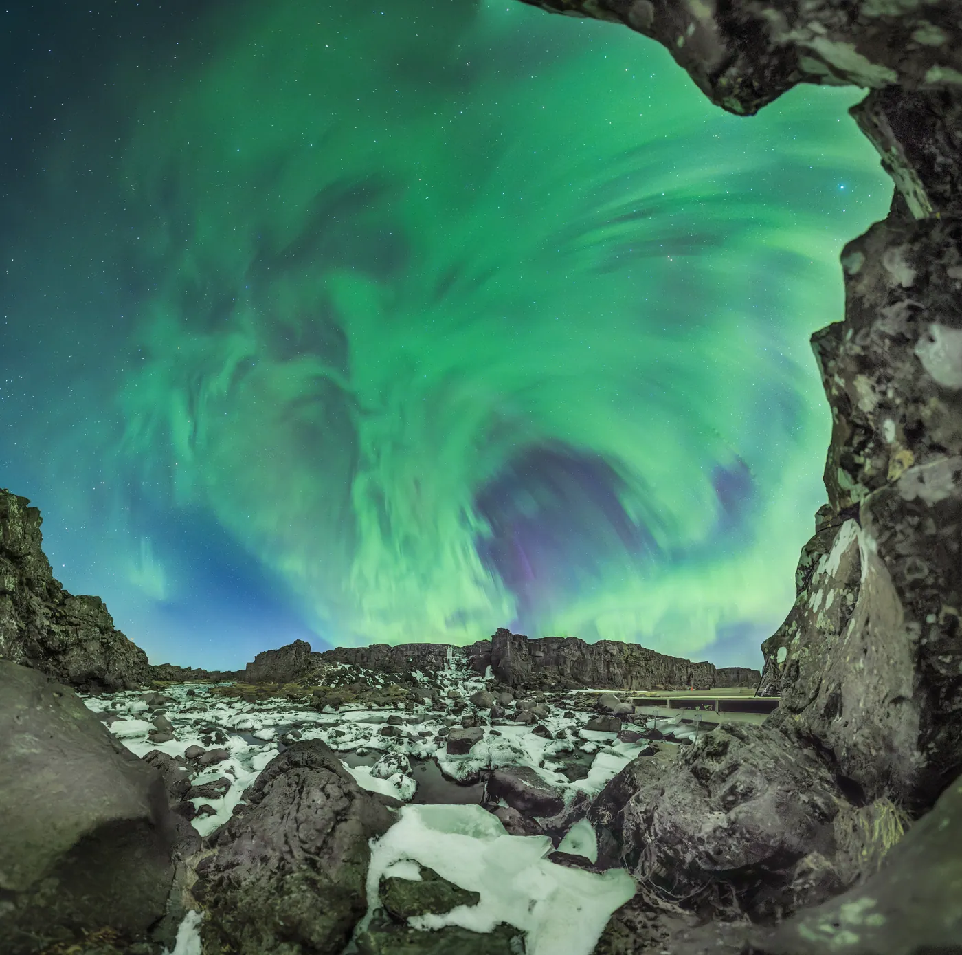 A green spiral of aurora seen through the opening of a rock cave.