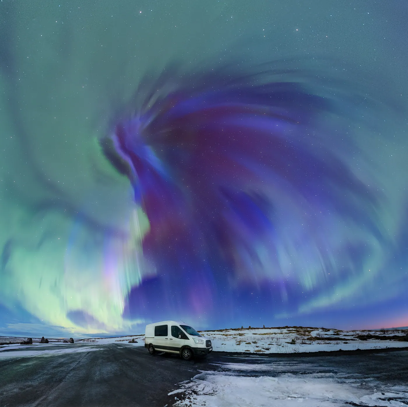 A violet and blue corona breaking open above a van parked on a snowy road.