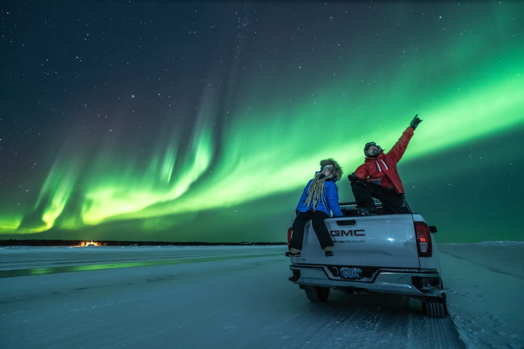 The two of them on the tailgate of a pick-up, pointing at bands of green aurora.