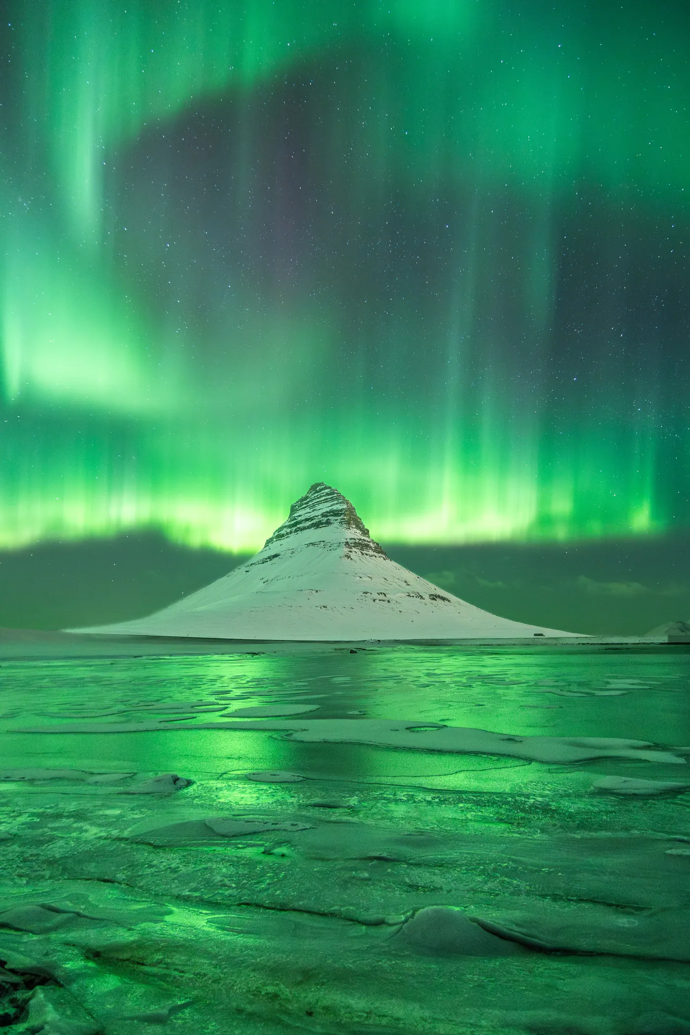 Green aurora over a conical mountain reflected in still water.