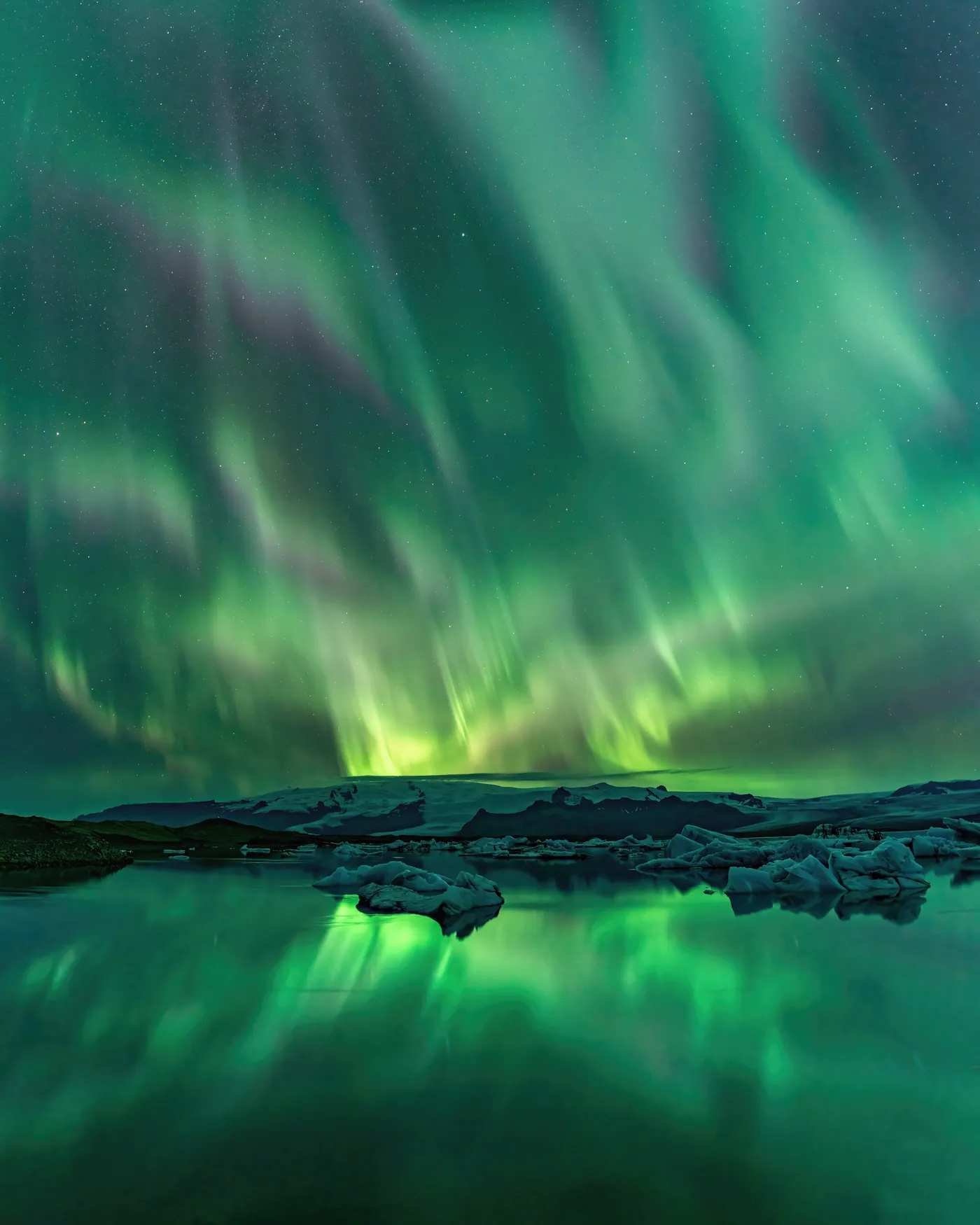 Green rays over a glacier lagoon, mirrored between the icebergs.