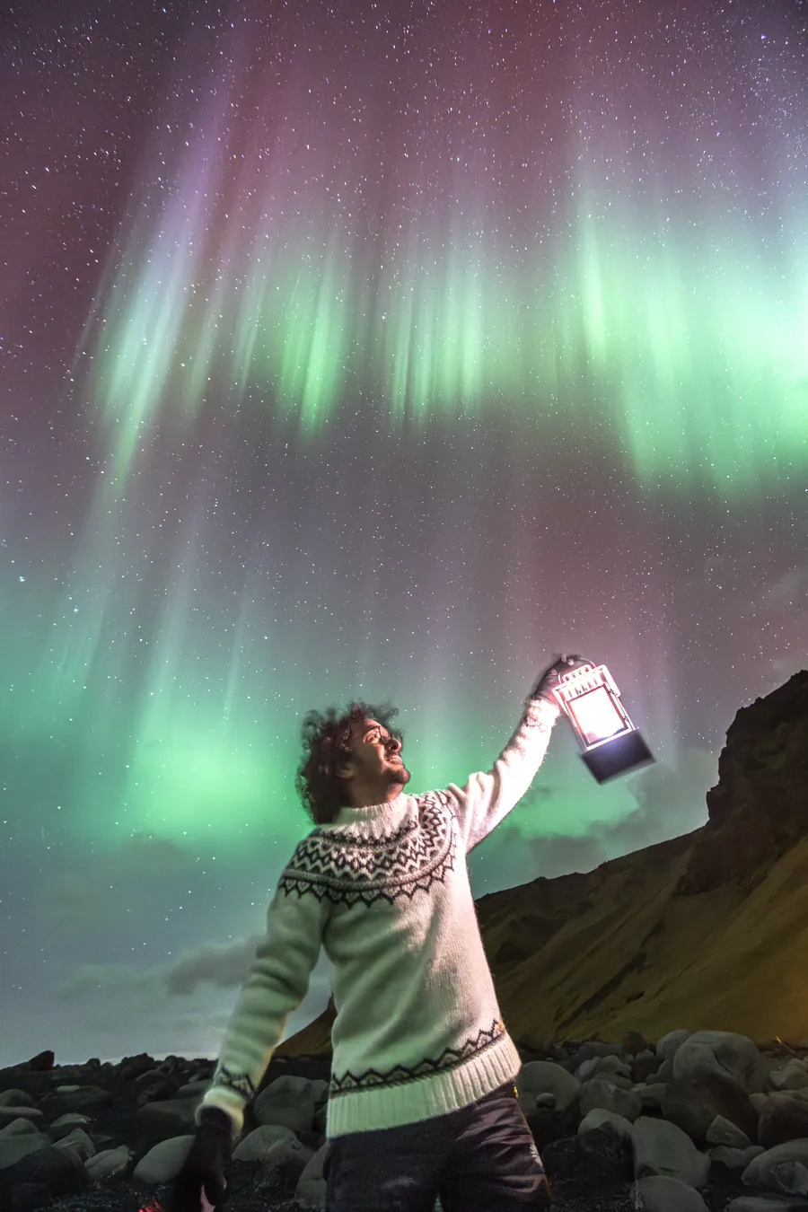 Mario Carvajal raising a lantern under green and violet aurora rays.